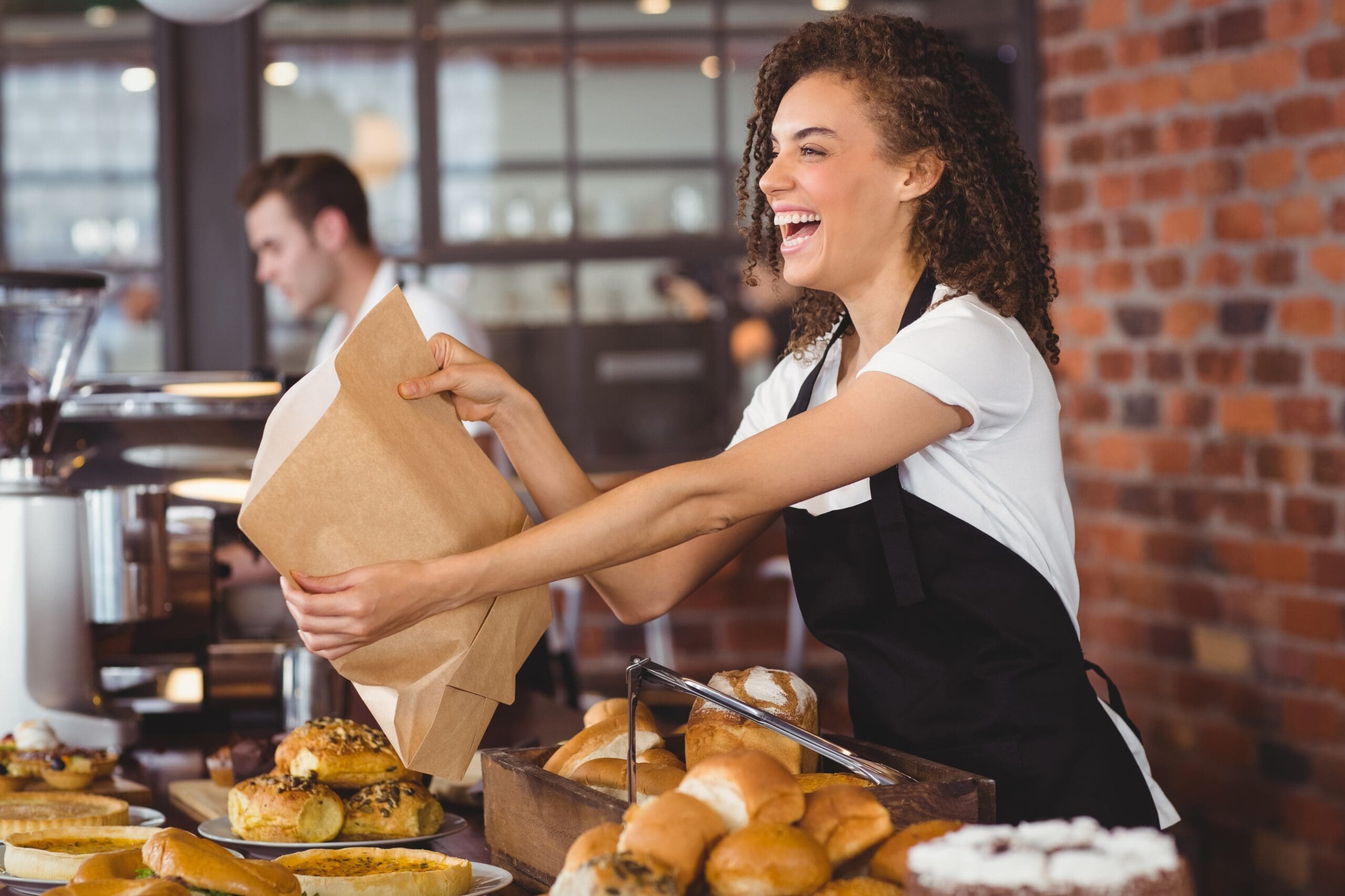 woman holding a paper bag in front of a counter full of pastries